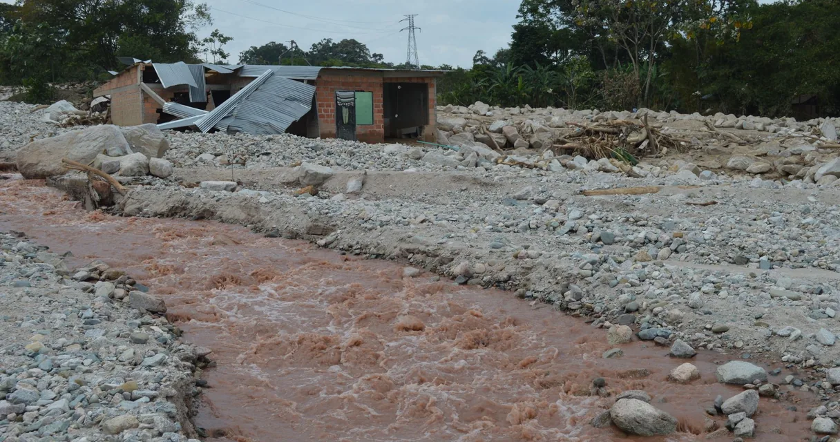 Rio com água barrenta ao lado de casas atingidas por enchente de rejeitos